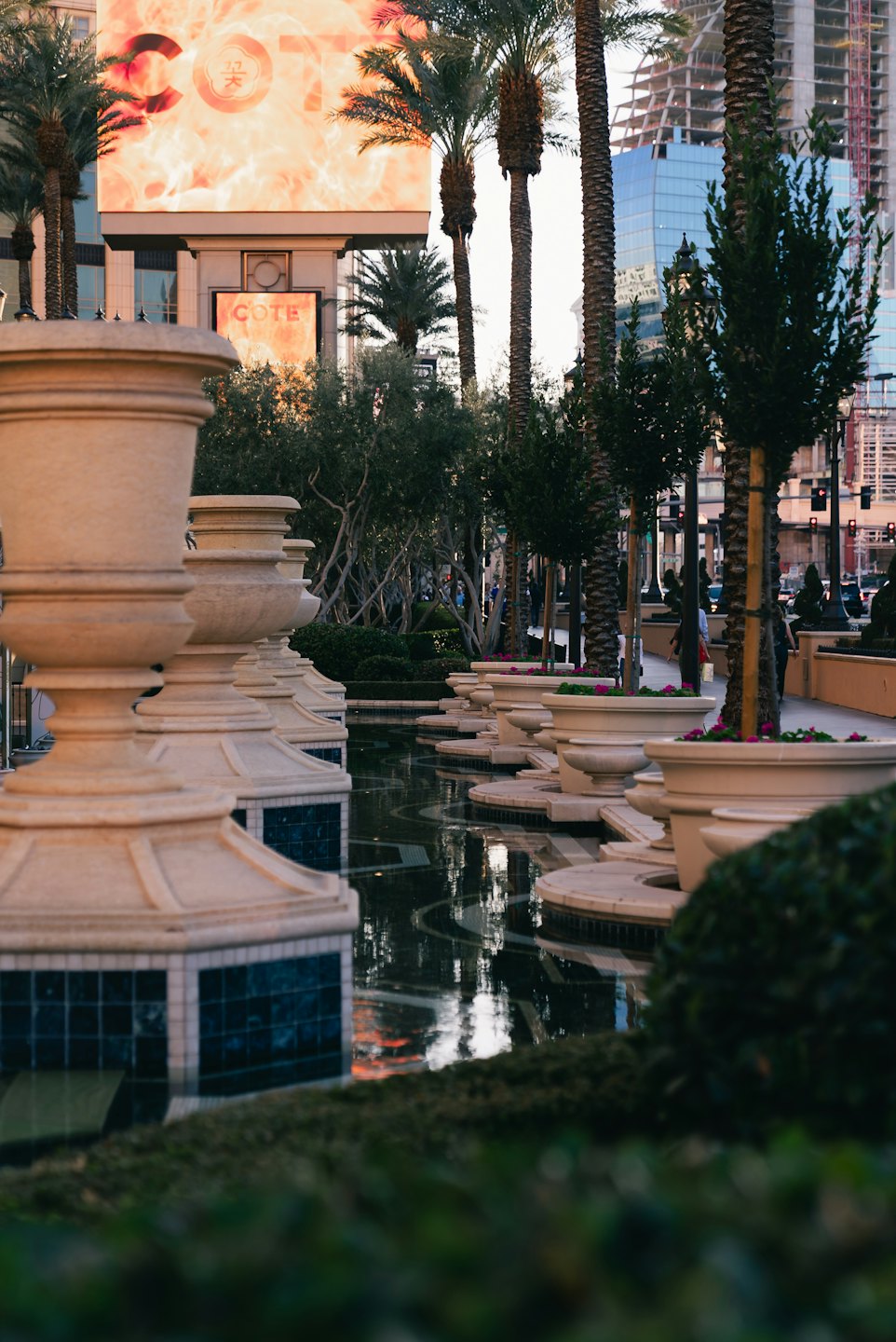 Macetas de piedra ornamentadas bordean un canal de agua en una plaza urbana.
