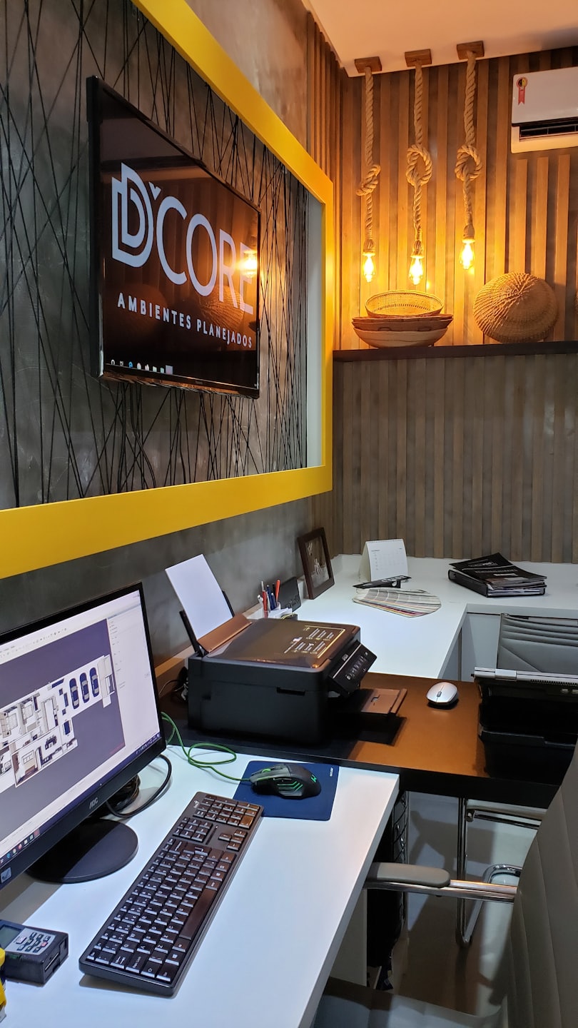 Oficina moderna con escritorios, computadoras mostrando planos y el logo de D'CORE.