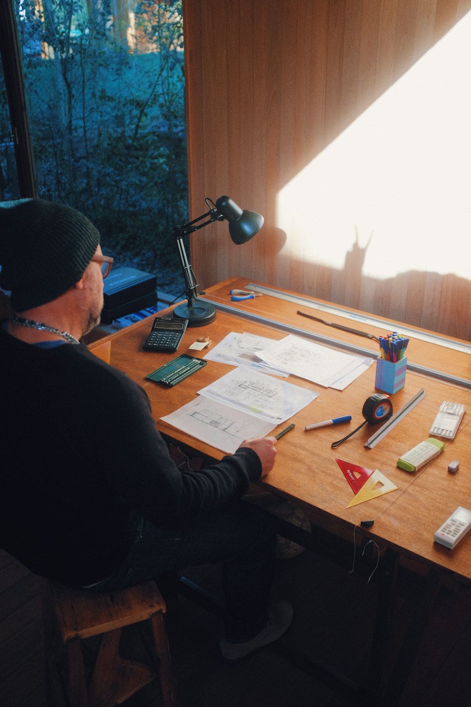 Arquitecto trabajando en planos sobre una mesa de dibujo iluminada por el sol.